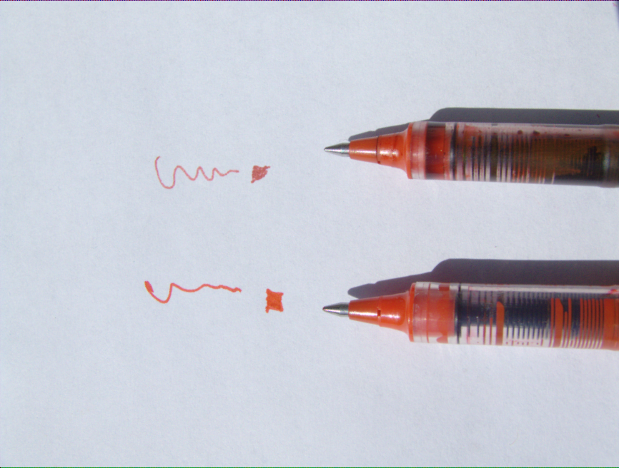 Two pens next to similar squiggles of red ink. The bottom is broader and brighter than the top one.