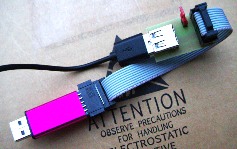 A USB programmer connected via a ribbon cable to a breakout board, connected to a USB cable that ends outside of the picture.
