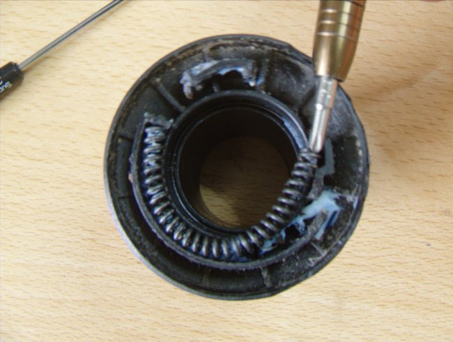 The moving part of X.0 10-gear with a spring partially in the groove. The other end of the spring is being poked by a screw driver, threatening to press it into the groove completely